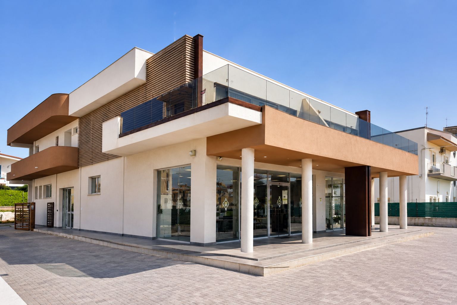 Ein modernes Gebäude mit zwei Obergeschossen, einem Glasvordereingang, weißen Säulen und einem Flachdach.