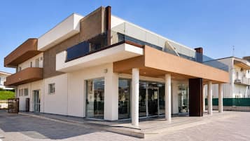 Ein modernes Gebäude mit zwei Obergeschossen, einem Glasvordereingang, weißen Säulen und einem Flachdach.