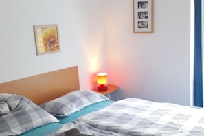 A bedroom with a bed, pillows, a nightstand with a lamp, and framed pictures on the wall. - Holiday home in Zingst with swimming pool (Zingst)