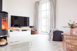 Un saló modern amb una llar de foc, televisió de pantalla plana, zona de seients confortable i una finestra gran amb cortines.