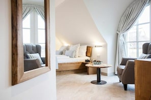 Ein modernes Schlafzimmer mit schrägem Dach, einem Bett mit Holz Kopfteil, einem runden Tisch mit Lampe und einem großen Spiegel an der Wand.