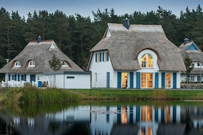 Eine Reihe von reetgedeckten Häusern mit weißen Wänden und blauer Fassade, gelegen am Ufer eines stillen Sees mit Spiegelungen.