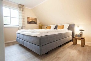 Ein Schlafzimmer mit einem Bett, einem Nachttisch, einem Fenster mit Vorhängen und einem Gemälde an der Wand.