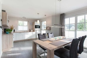 Eine moderne Küche mit weißen Schränken, einem Esstisch mit Stühlen und einem großen Fenster für natürliches Licht.