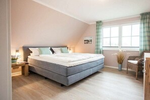A bedroom with a bed, a bedside table, a chair, a window with curtains, and a picture on the wall. - Holiday home with 2 bedrooms (Fuhlendorf)