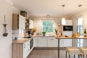 A modern kitchen with white cabinetry, a central island, and pendant lighting. - Holiday home with 2 bedrooms (Fuhlendorf)