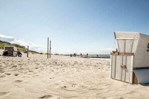 A beach with a wicker chair and a wooden structure, possibly a beach hut, in the foreground. - Holiday home with 2 bedrooms (Fuhlendorf)