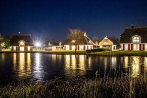 Een nachtzicht van een landgoed aan een meer, met verlichte gebouwen die in het water worden weerspiegeld.