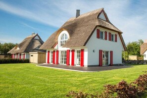Et traditionelt hus med stråtækt tag, hvide vægge og røde skodder.