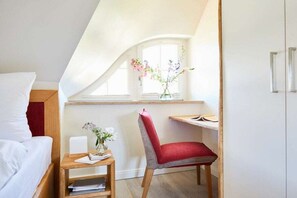 Ein Schlafzimmer mit Bett, Schreibtisch mit Stuhl, Fenster mit Blumen und einem Kleiderschrank.