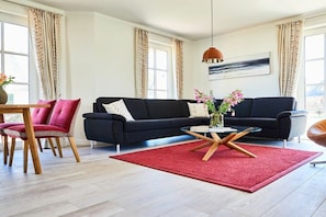 Ein modernes Wohnzimmer mit einem schwarzen Sofa, einem roten Teppich und einem Couchtisch mit einer Blumenvase.