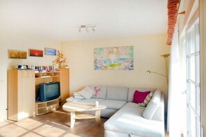 Ein Wohnzimmer mit einer Couch, einem Couchtisch, einem Fernseher auf einem Holzboden und einem Bild an der Wand.