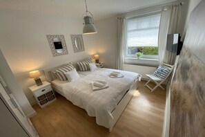 A bedroom with a large bed, bedside lamps, a TV, and a window with curtains. - Holiday apartment with 2 bedrooms (Travemünde)
