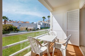 A balcony with a white table and chairs, a view of a green lawn, and white buildings in the background. - Casa da Galé Pool Terrace (Albufeira)