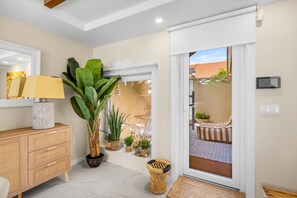 Un interior moderno con un mueble de madera, una planta grande en maceta, una silla de mimbre y vistas a través de un ventanal.