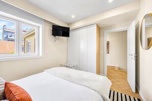 A bedroom with a bed, a TV mounted on the wall, a wardrobe, and a door leading to another room. - Charminn Mar (Ovar)