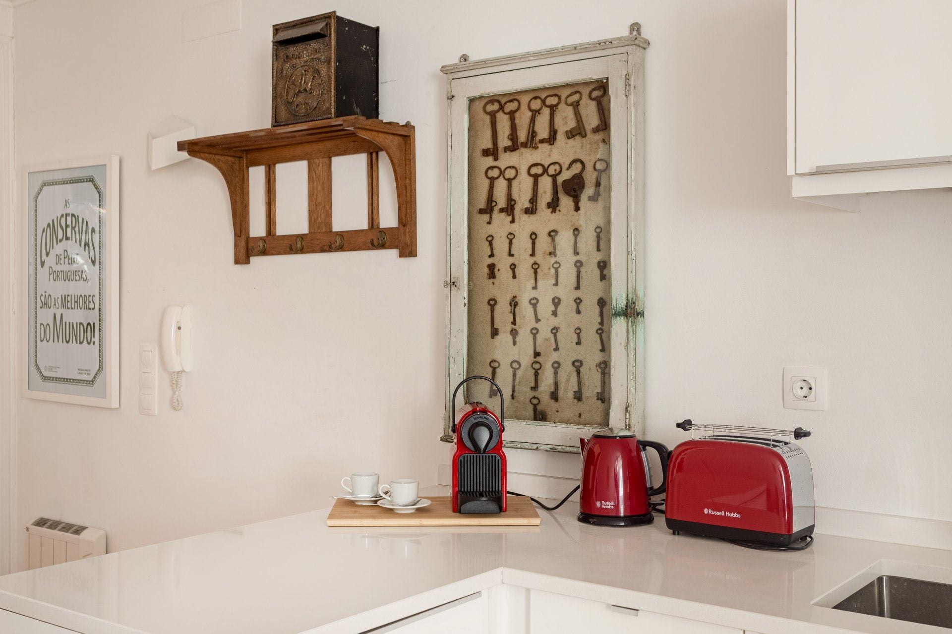 Een keuken met een houten kastje, een sleutelrek aan de muur, een vintage telefoon, een rode toaster en een waterkoker op het aanrecht.