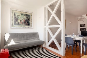 Een kamer met een grijze bank, een zwart-wit gestreept vloerkleed, een eettafel met stoelen en een ingelijst schilderij aan de muur.