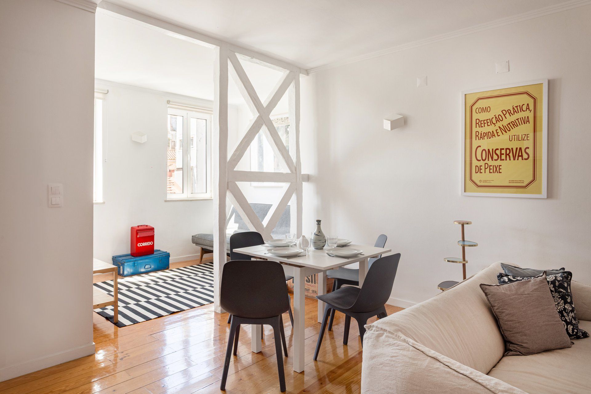 Een eethoek met een tafel voor twee personen, stoelen, een vaas en een ingelijste poster aan de muur.