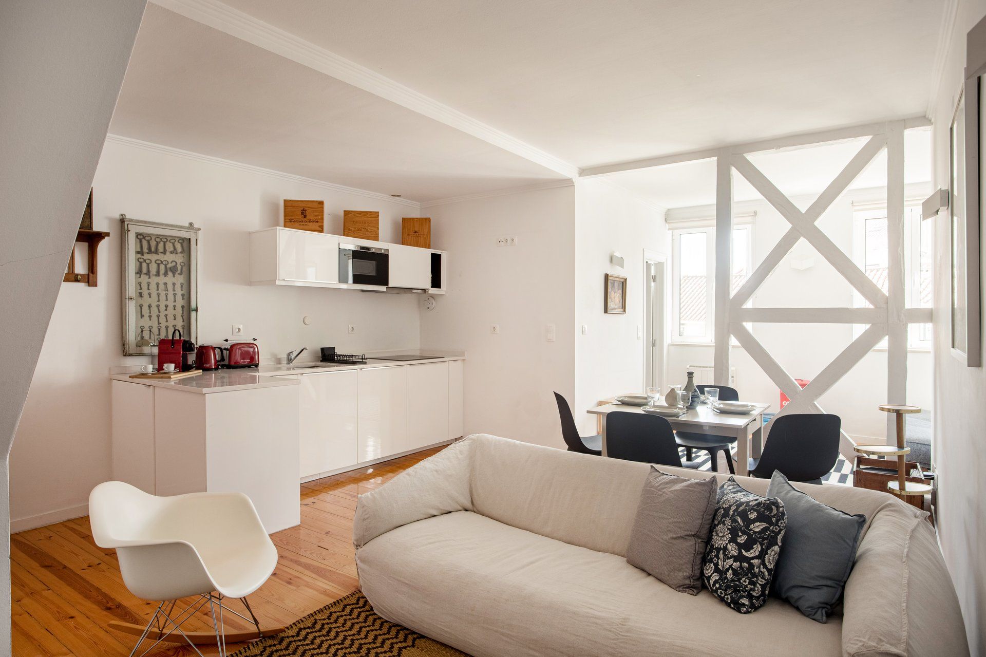Een moderne woonkamer met een bank, een eethoek met stoelen, een keuken met witte kastjes en een groot raam met verstevigingen.
