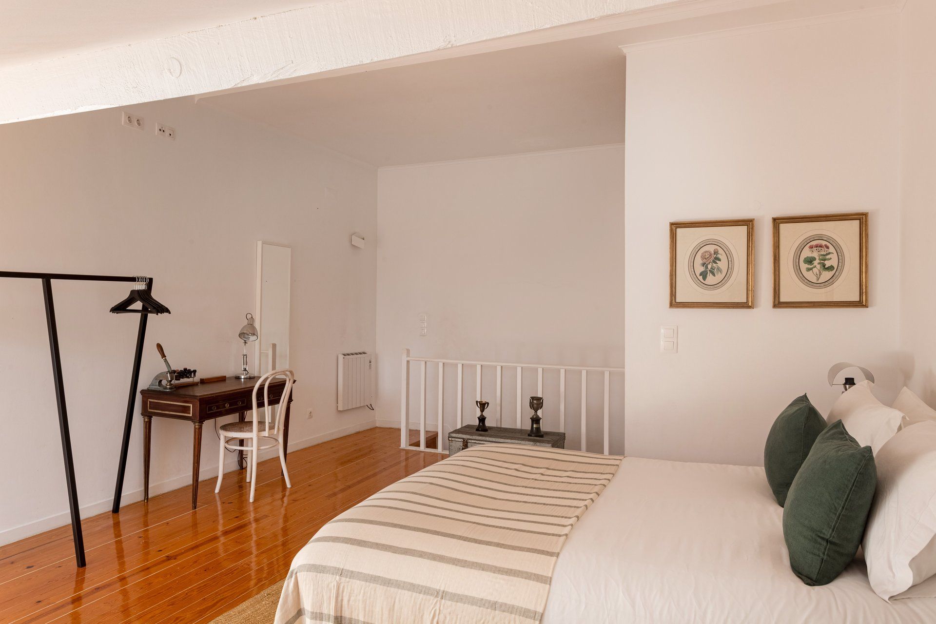 Een slaapkamer met een bed, een bureau, een stoel, een radiator en twee afbeeldingen in lijsten aan de muur.