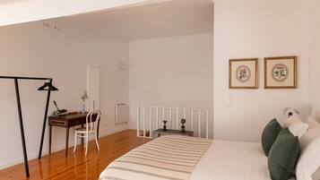 Een slaapkamer met een bed, een bureau, een stoel, een radiator en twee afbeeldingen in lijsten aan de muur.