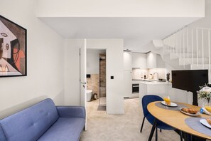 A modern living room with a blue sofa, a dining table with breakfast items, and a staircase leading to a kitchen area. - Skylight Loft Terracotta Collection (Porto)