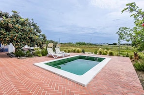 A swimming pool with two lounge chairs, surrounded by a brick patio and greenery. - Melides Nature, Beach Golf Retreat (Santiago do Cacém)