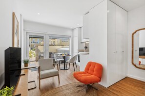A modern living room with a TV, seating, a dining area, and a view of the outside. - Porto Garden Private Patio Studio (Porto)