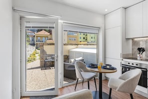 A modern kitchen with a dining area, a sliding glass door leading to a balcony, and a view of neighboring buildings. - Porto Garden Private Patio Studio (Porto)