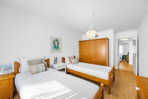 Un dormitorio con dos camas, un armario de madera, una mesita de noche, una lámpara y un cuadro en la pared.