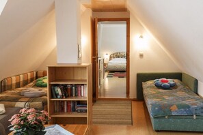 A compact room with a loft bed, a small seating area with a sofa, a bookshelf, and a door leading to another room. - Taun coupling current (Born a. Darß)