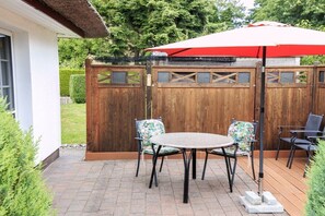 An outdoor patio with a round table and chairs, a wooden fence, and a red umbrella. - Taun coupling current (Born a. Darß)