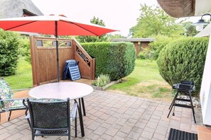 A patio with a round table and chairs, a red umbrella, a wooden deck, and a black grill. - Taun coupling current (Born a. Darß)