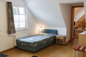 A dormitory room with a single bed, a nightstand, a window with curtains, and a wooden staircase. - Taun coupling current (Born a. Darß)