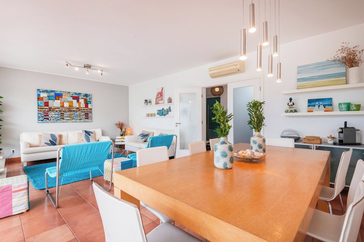 Un salón moderno con una mesa de comedor de madera, sofás blancos y un cuadro abstracto de colores.