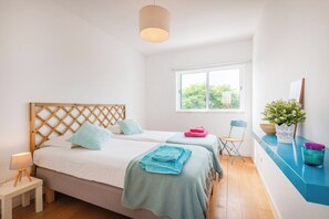 A bedroom with two beds, a window, a bedside table, a chair, and a potted plant. - Sunny 3BR Villa Prainha Clubhouse (Portimão)