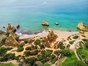 An aerial view of a coastal area with rocky formations, a sandy beach, and green vegetation. - Sunny 3BR Villa Prainha Clubhouse (Portimão)