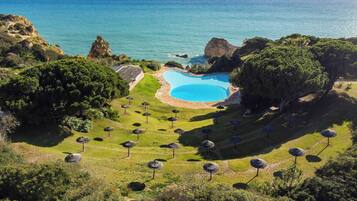 Una piscina rodeada de árboles y sombrillas, con vista al océano.