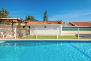 Ein Pool mit weißem Zaun, einer überdachten Terrasse und einem Gebäude mit rotem Ziegeldach.