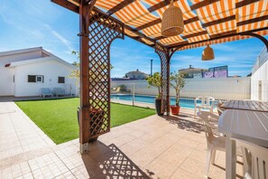 Ein überdachter Patio-Bereich mit Pool, Rasenfläche und einem weißen Gebäude im Hintergrund.