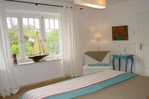 Une chambre à coucher avec un lit, une fenêtre avec des rideaux, une décoration sur le thème de la voile, une lampe et un tableau.