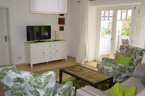 Ein Wohnzimmer mit Fernseher, weißem Schrank, grünem Sofa und einem Couchtisch.