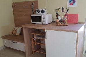 A kitchenette with a microwave, a small shelf, and a wine rack with bottles. - with direct lake access (Trams)