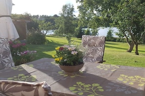 A table set outdoors with a floral tablecloth, a potted plant with flowers, and a chair with a patterned cushion. - with direct lake access (Trams)