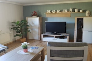 A living room with a television, a dining table with a plant, and a sofa. - with direct lake access (Trams)