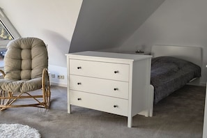 A bedroom with a white dresser, a rocking chair, a bed with a gray blanket, and a white rug. - Holiday apartment with 1 bedroom (Moisburg)