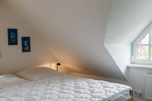Ein Schlafzimmer mit einem Bett, einem Fenster und zwei an der Wand befestigten Bilderrahmen.