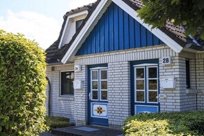 Ein zweistöckiges Gebäude mit blau-weißer Fassade, einer gut sichtbaren Nummer '2B' an der Seite und einem kleinen Fenster mit Blumenmuster.