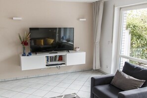 A living room with a mounted TV, a sofa, and a window with curtains. - Holiday apartment with 2 bedrooms (Born a. Darß)